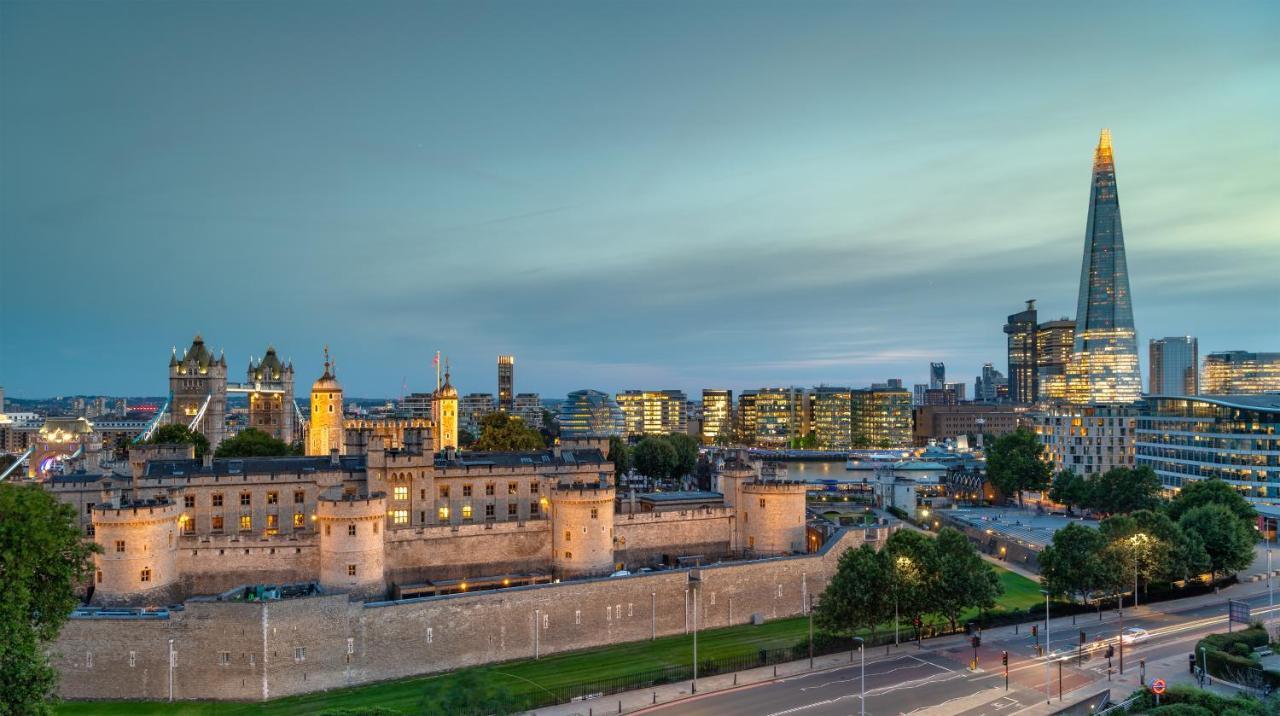 Tower Suites By Blue Orchid Londra Exterior foto The photo shows a view of a historical site and modern skyline. In the foreground, there is a prominent historical building, likely a castle or fortress, featuring tall towers and a stone wall. This structure is set against a backdrop of contemporary