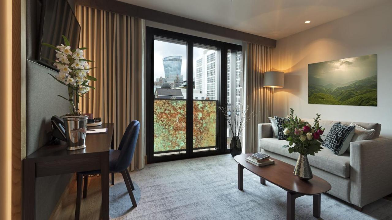 Tower Suites By Blue Orchid Londra Exterior foto The photo shows a modern and well-lit living space. There is a comfortable sofa with decorative cushions, a small coffee table in front of it, and a floor lamp providing additional lighting. Beside the sofa, there are decorative plants and a vase wit