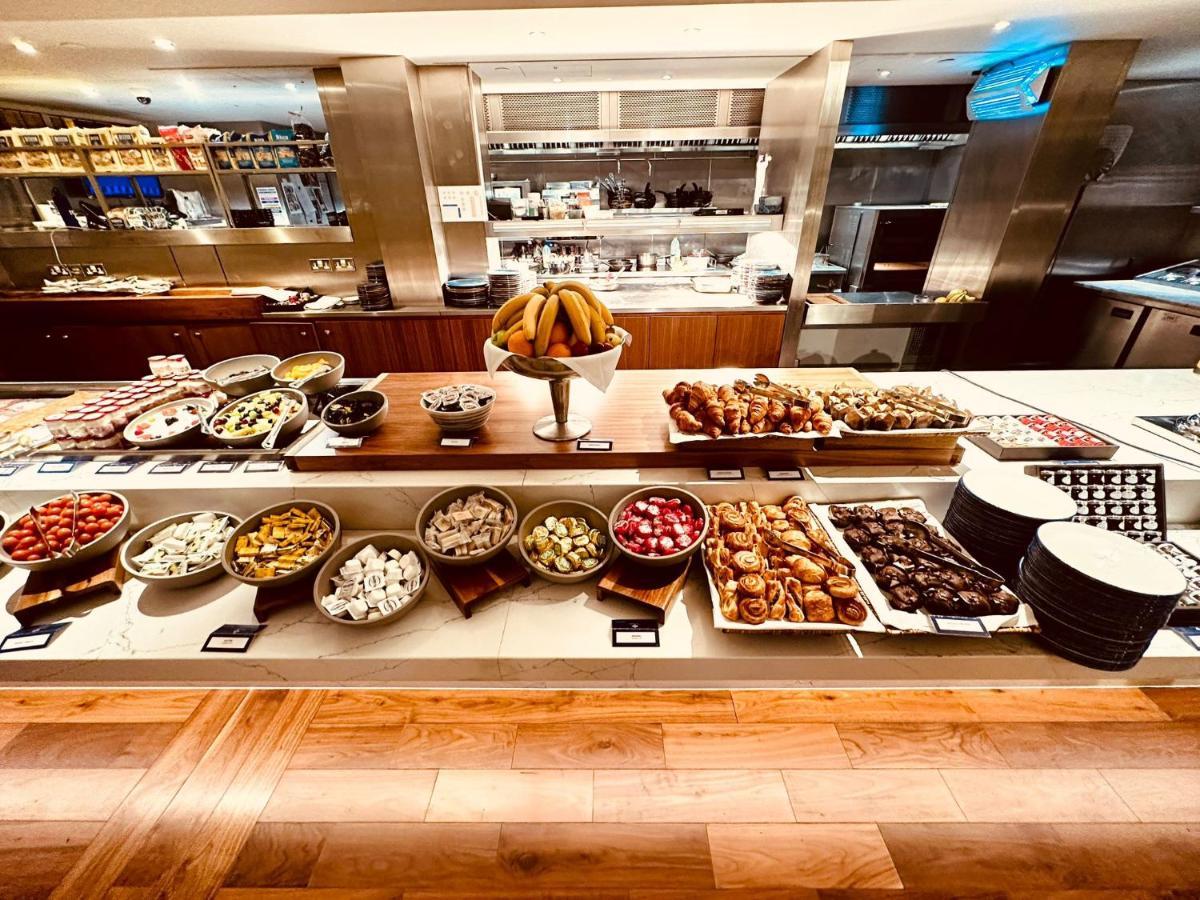 Tower Suites By Blue Orchid Londra Exterior foto The photo displays a beautifully arranged buffet featuring a variety of food items. There are several bowls and platters filled with colorful fruits, pastries, and desserts. In the center, a large bowl of bananas is prominently placed. Surrounding th