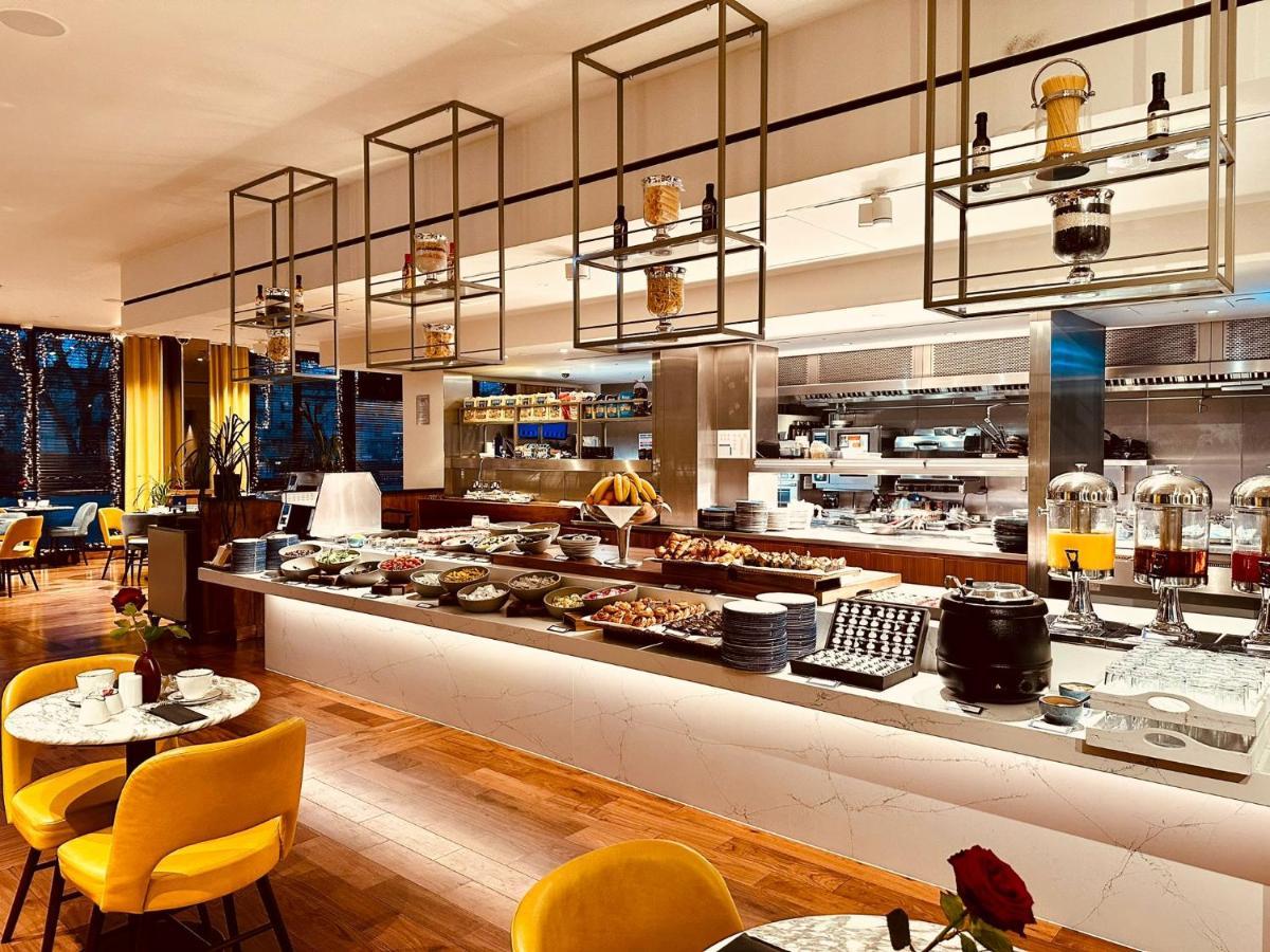 Tower Suites By Blue Orchid Londra Exterior foto The photo shows a modern restaurant interior featuring a buffet layout. The space has a sleek design with wooden flooring and a bright, open atmosphere.  

The buffet counter is richly arranged with various dishes and food items, likely for a breakfa