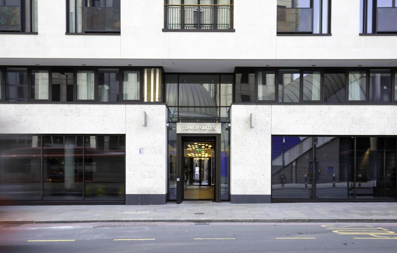 Tower Suites By Blue Orchid Londra Exterior foto The image shows the entrance of a modern building, characterized by its minimalist architectural design. The facade features a combination of large glass windows and smooth stone surfaces. The entrance is framed by glass doors, flanked by stylish lig