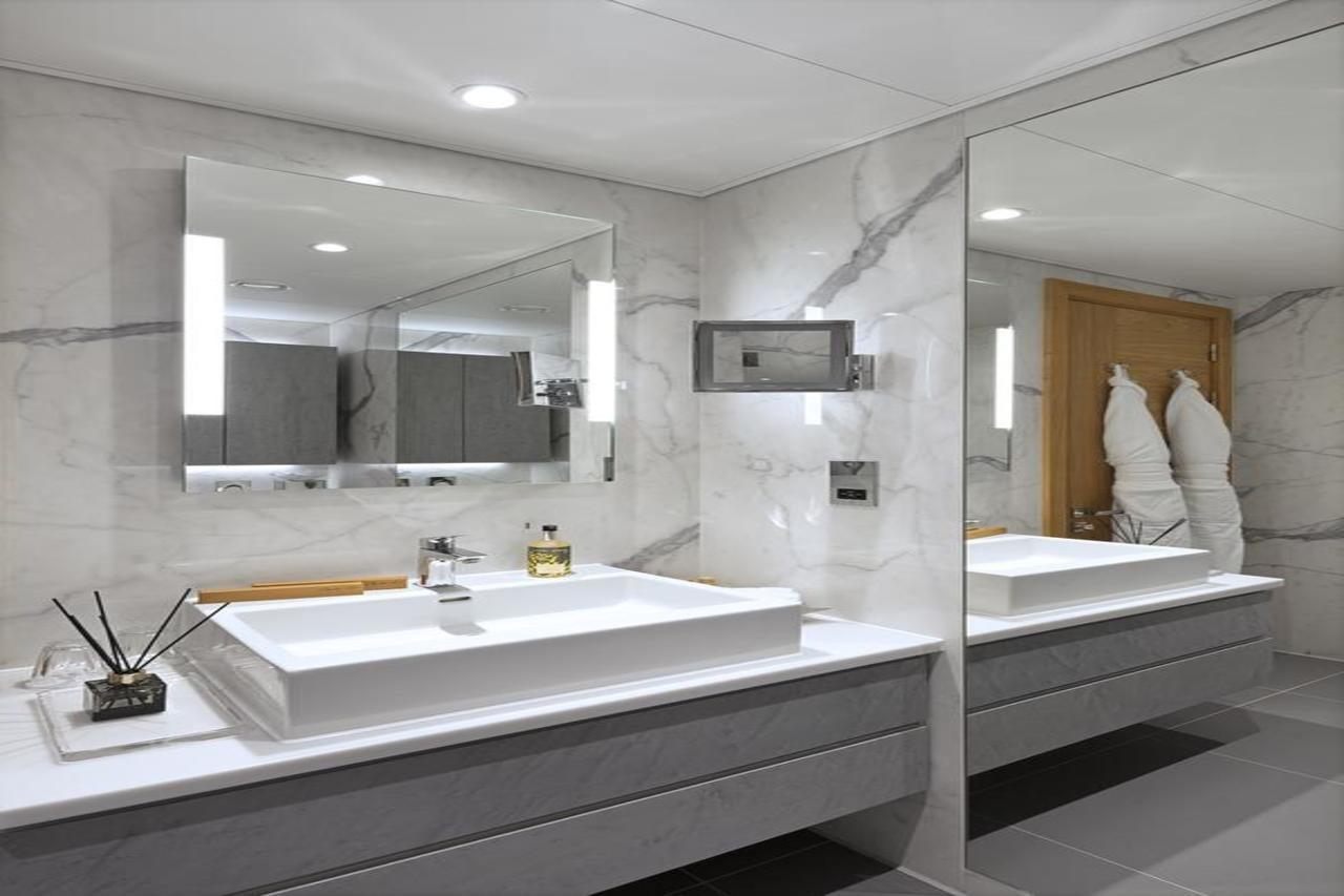 Tower Suites By Blue Orchid Londra Exterior foto The photo shows a modern bathroom featuring a sleek design. 

- **Vanity Area**: There is a rectangular sink set into a white countertop, paired with a minimalist faucet. 
- **Mirrors**: Above the sink, there is a large mirror that reflects the entir